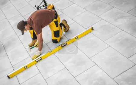 Caucasian Construction Worker Building Patio Concrete Floor. Finishing Touches with a Soft Hammer