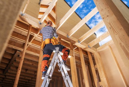 Foto de Trabajador del contratista dentro del marco de madera recién construido de la casa que termina algunos elementos - Imagen libre de derechos