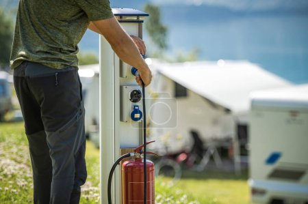 Téléchargez les photos : Camping-car RV propriétaire attachant le câble d'alimentation au poteau électrique de camping pendant le séjour de camping - en image libre de droit