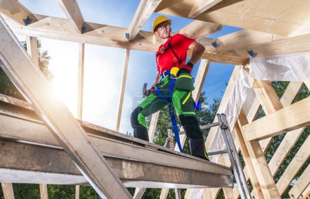 Téléchargez les photos : Travailleur du chantier de construction caucasien dans sa quarantaine Bâtiment Maison en bois cadre de toit. Travailler à partir d'échafaudages. - en image libre de droit
