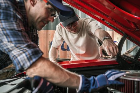 Téléchargez les photos : Deux amateurs de voitures musculaires classiques caucasiens travaillant sur le moteur de voiture - en image libre de droit