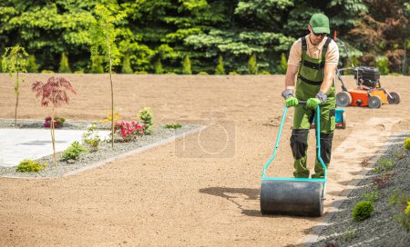 Photo for Professional Caucasian Landscaper Preparing Backyard Garden Soil For Grass Seeding Using Compactor - Royalty Free Image