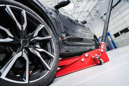 Foto de Vehículo moderno levantado en un gato de coche hidráulico rojo dentro del almacén de servicio automático del concesionario - Imagen libre de derechos