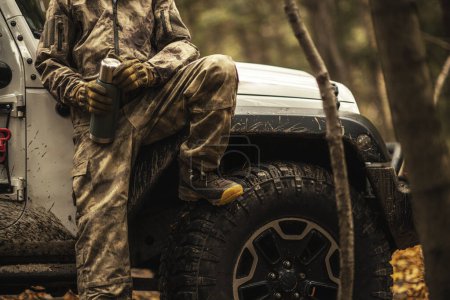 Téléchargez les photos : Porter le camouflage Animal Hunter Rester à côté de son véhicule AWD avec café Thermos - en image libre de droit