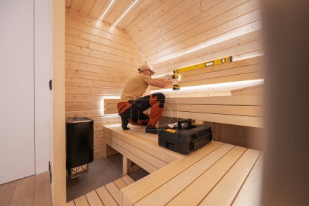 Téléchargez les photos : Homme caucasien construisant moderne LED éclairé sauna finlandais résidentiel. Accueil Thème SPA. - en image libre de droit