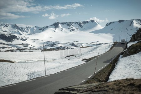 Téléchargez les photos : Camionnette Camper Classe C sur une route de montagne norvégienne au début de l'été - en image libre de droit