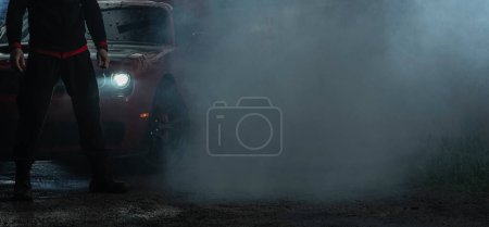 Foto de Moderno coche muscular y un conductor cubierto por el humo después de agotamiento pesado. Espacio de copia del lado derecho. Tema automotriz. - Imagen libre de derechos
