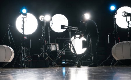 Foto de Un hombre que ensambla el vídeo moderno potente del led y la iluminación fotográfica dentro del estudio oscuro de la producción - Imagen libre de derechos