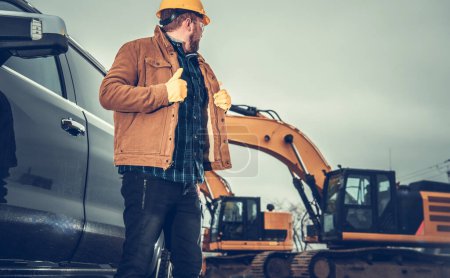 Téléchargez les photos : Superviseur du chantier de construction caucasien vérifiant l'équipement lourd au sol - en image libre de droit