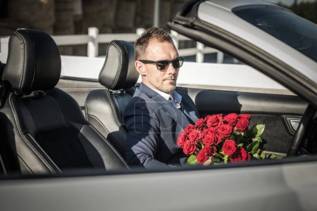 Téléchargez les photos : Homme élégant caucasien avec des roses rouges en attente de sa date dans un véhicule convertible - en image libre de droit