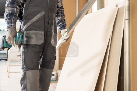 Foto de Trabajador del sitio de construcción con un conductor de taladro en su mano preparándose para construir otra pared de paneles de yeso - Imagen libre de derechos