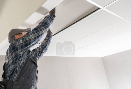 Téléchargez les photos : Travailleur sur chantier Installation d'un plafond suspendu à l'intérieur d'un bâtiment commercial - en image libre de droit