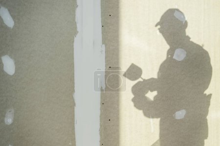 Téléchargez les photos : Bâtiment Intérieur cloisons sèches Patching thème avec une ombre d'un travailleur. Industrie de la construction Thème. - en image libre de droit