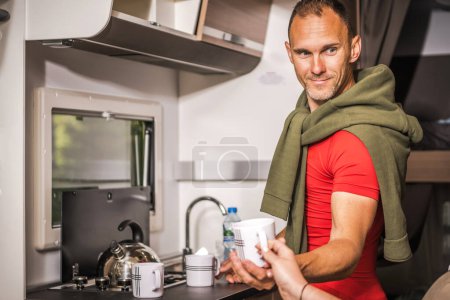 Happy Caucasian Man Serving Hot Tea While Standing Next to Camper Van Kitchen. Summer RV Road Trip