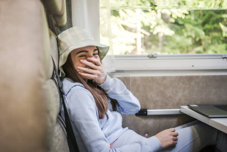Téléchargez les photos : Heureuse fille caucasienne riant tout en s'asseyant à l'intérieur d'un camping-car. Thème vacances d'été. - en image libre de droit