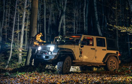 Téléchargez les photos : Recherche d'urgence de personnes disparues dans une forêt pendant les heures de nuit. Membre d'équipage regardant sur une carte debout à côté de son véhicule de traction intégrale. - en image libre de droit