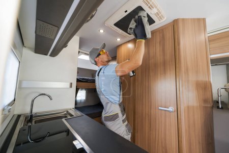 Trabajador caucásico limpieza de techo montado en la unidad de aire acondicionado en una casa de alquiler de RV Motor. Tema de mantenimiento de vehículos recreativos.