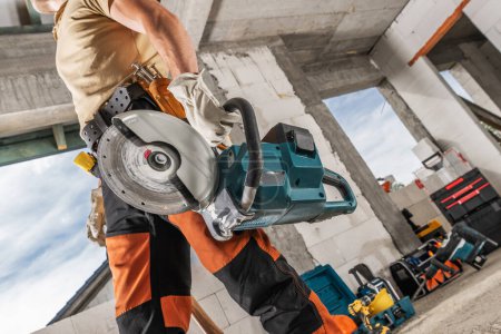 Construction Worker with a Professional Circular Saw in His Hand Walking Along Construction Site