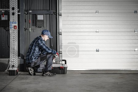 Téléchargez les photos : Technicien caucasien dans la quarantaine qui entretient la porte de garage du quai commercial. Thème industriel. - en image libre de droit