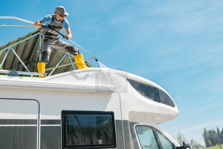 Téléchargez les photos : Propriétaire de VR Laver son camping-car moderne Van Roof à l'aide de laveuse sous pression - en image libre de droit