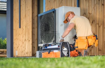Photo for HVAC worker working on a modern heat pump outside a house. - Royalty Free Image