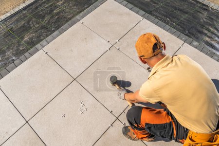 Photo for Caucasian worker is installing tiles on a concrete garden patio floor - Royalty Free Image