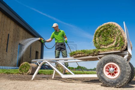Caucasian garden worker installing grass turfs and watering soil