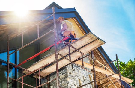 Photo for Construction worker making chimney repairs on a building using scaffolding. - Royalty Free Image