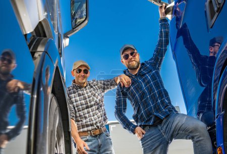 Téléchargez les photos : Deux heureux chauffeur de camion semi caucasien debout à côté de semi-camions bleus. - en image libre de droit