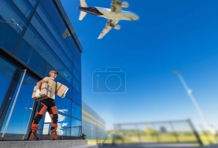 Téléchargez les photos : Courier se tient devant un bâtiment avec un avion en arrière-plan. - en image libre de droit