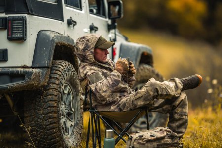 Téléchargez les photos : Homme caucasien en camouflage assis à côté d'un véhicule utilitaire sport - en image libre de droit