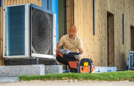 Photo for HVAC technician working on a modern heat pump in front of a building. - Royalty Free Image