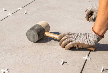 Téléchargez les photos : Personne travaillant avec un marteau sur le sol du patio carrelé. - en image libre de droit