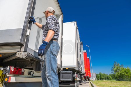 Photo for Caucasian semi truck driver opening back doors of a truck trailer. Transportation industry - Royalty Free Image