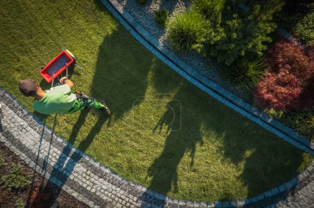 Téléchargez les photos : Travailleur du jardin utilise un distributeur d'engrais pour nourrir l'herbe vue aérienne. - en image libre de droit