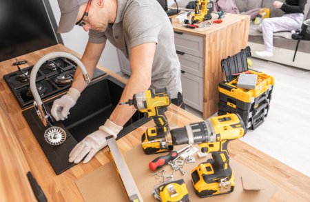 Caucasian man is diligently working on a table, surrounded by various power tools that he is using for his task.
