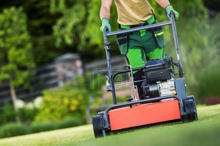 Téléchargez les photos : Paysager aère la pelouse avec un aérateur à essence dans une cour résidentielle par une journée ensoleillée. - en image libre de droit