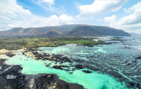 Entdecken Sie das beschauliche Caleton Blanco auf Lanzarote, wo vulkanische Felsen türkisfarbenes Wasser vor einer dramatischen Bergkulisse wiegen.