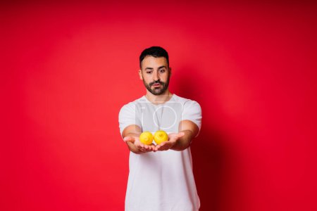 Foto de Portrait of young bearded man holding lemons in both hands on an isolated red background - Imagen libre de derechos