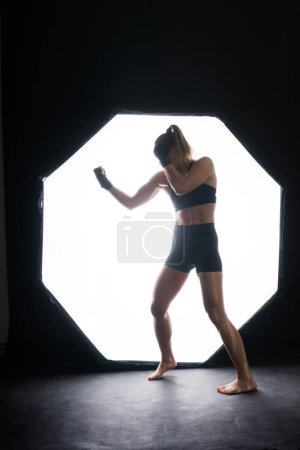 Photo for Cool female fighter in boxing bandages trains in a studio. Mixed martial arts. - Royalty Free Image