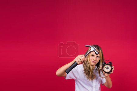 Foto de Joven chica rubia sosteniendo un reloj despertador y martillo sonriendo y riendo en voz alta. - Imagen libre de derechos