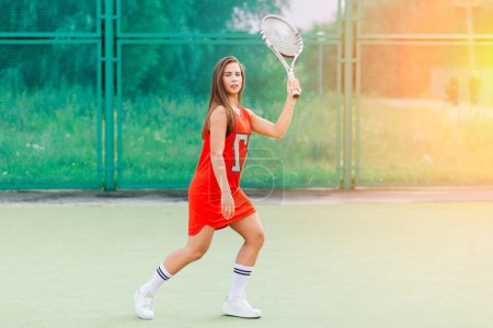 Téléchargez les photos : Belle joueuse de tennis sur un court de tennis en robe rouge. - en image libre de droit