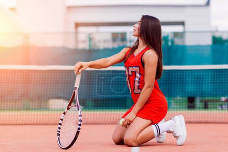 Téléchargez les photos : Belle joueuse de tennis sur un court de tennis en robe rouge. - en image libre de droit
