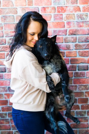 Téléchargez les photos : Joyeux dame brune dans une tenue décontractée étreignant chien de compagnie mudi, fond de studio. - en image libre de droit