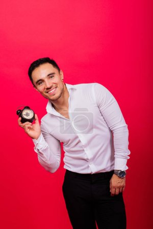 Emotionaler junger Mann mit Uhr auf rotem Hintergrund. Verspätetes Konzept