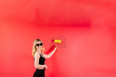 Téléchargez les photos : Jeune femme avec brosse à rouleaux sur fond blanc rouge Instruments accessoires pour salle de rénovation - en image libre de droit