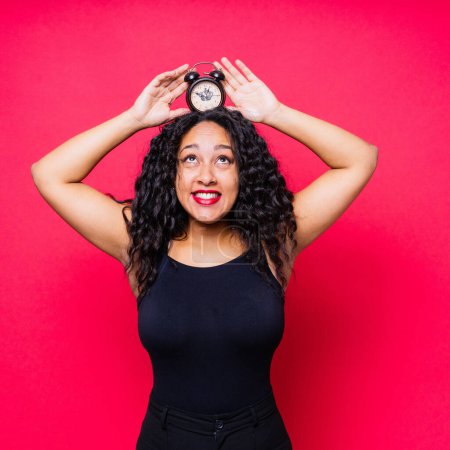 Lächelnde junge afrikanisch-amerikanische Frau posiert isoliert auf rotem Hintergrund mit Uhr