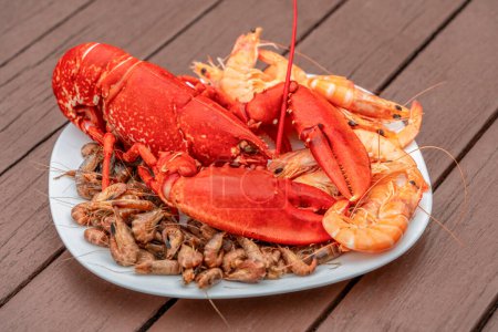 Closeup shot of a cooked lobster and some other crayfish on a plate on wooden planks