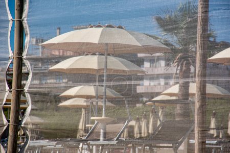 Téléchargez les photos : Station balnéaire, avec chaises longues et parasols, vue de la plage à travers un filet de protection - en image libre de droit