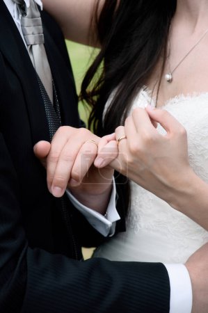 Foto de Las manos de la pareja recién casada con rosas entrelazadas y anillos de boda prominentemente exhibidos - Imagen libre de derechos